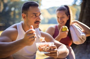 Pareja en el parque tomando un descanso y comiendo una comida saludable. Ensalada y manzana. La atención se centra en el hombre.