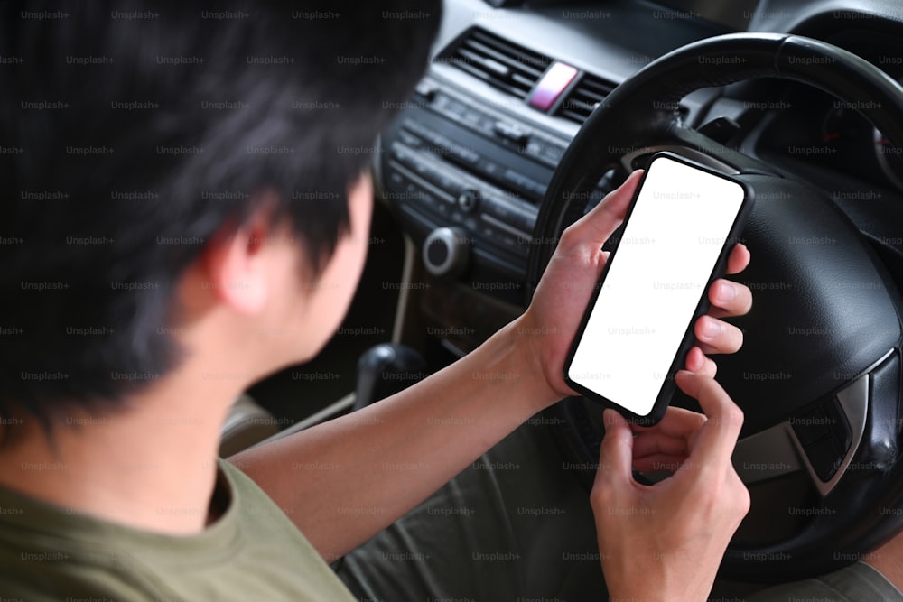 Jeune homme assis dans une voiture et utilisant un téléphone portable.
