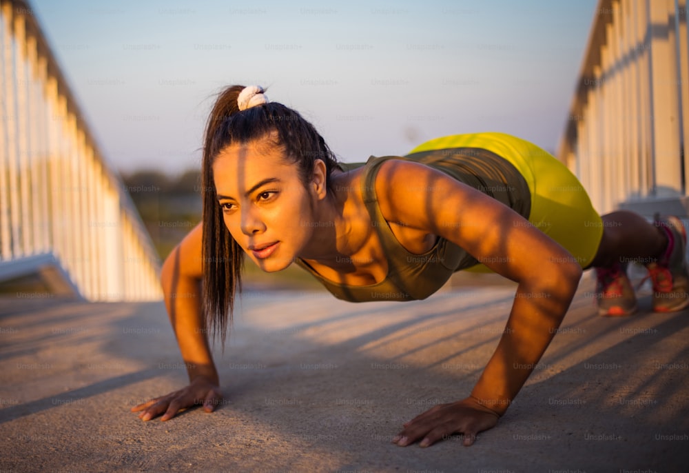African sportswoman doing push-ups on the bridge. Confident strong fitness female.