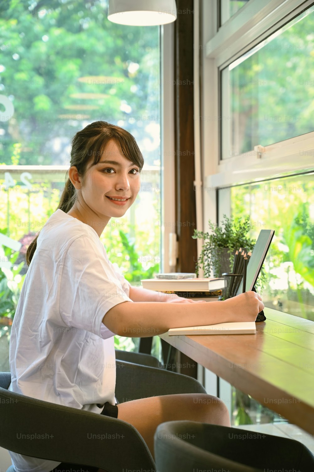 Cheerful young female freelancer working with computer tablet at coffee shop.