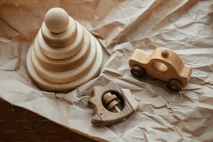 Moderne Naturholzpyramide mit Ringen, Beißelhigel und Autospielzeug auf Bastelpapier auf Holztisch. Umweltfreundliches plastikfreies Spielzeug für Kleinkinder. Stilvolles einfaches Holzspielzeug für Kinder