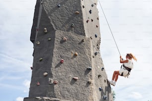 Little girl in casual white clothes training rock climbing outdoors.