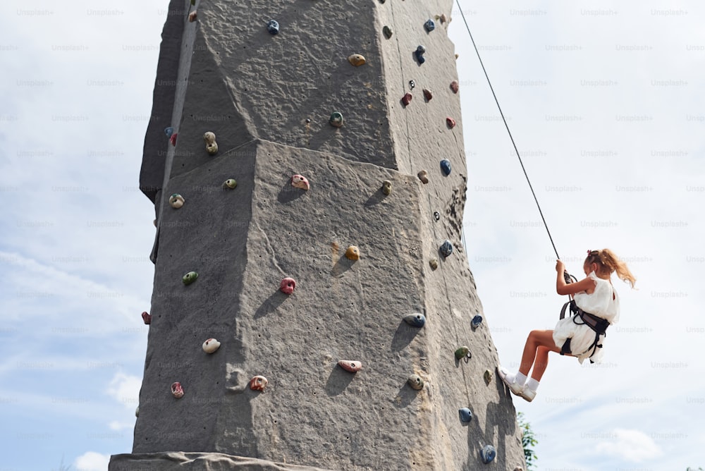 Little girl in casual white clothes training rock climbing outdoors.