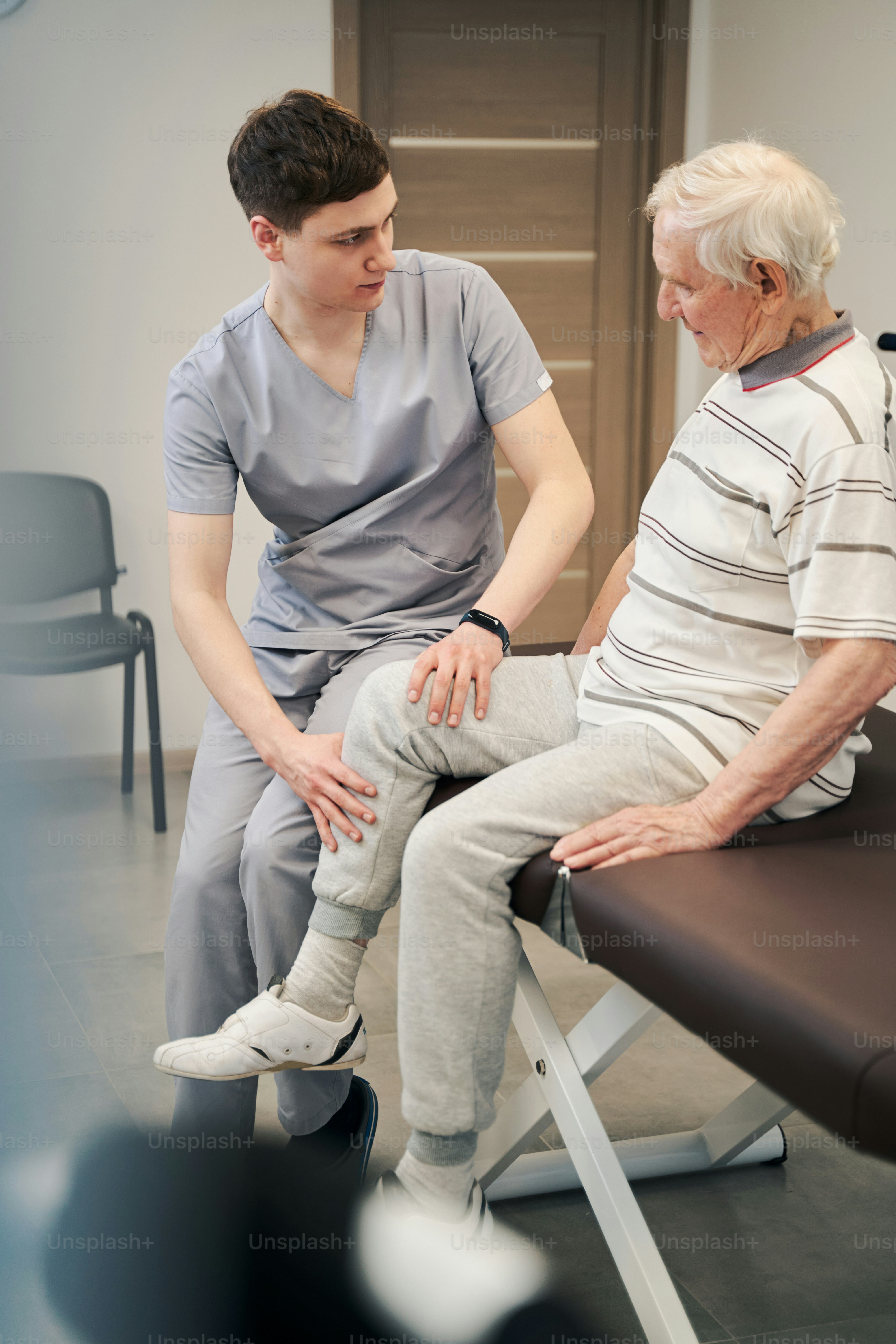 Orthopedic surgeon laying his hands on aging man right leg while inspecting its state and looking at patient face
