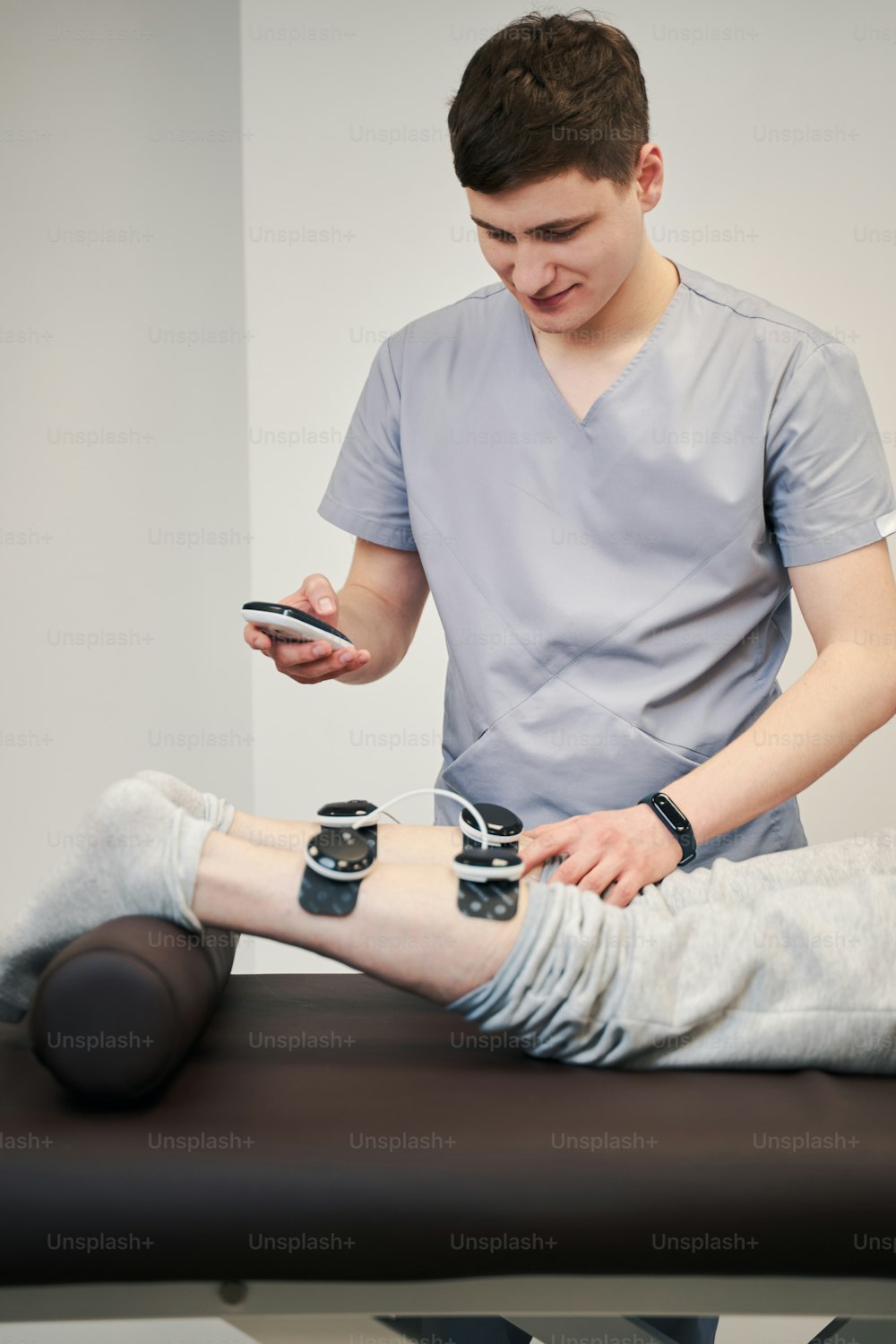 Elettrodi a scatto professionali medici che premono sulla gamba della persona mentre toccano il display dell'unità di stimolazione muscolare