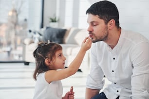 Girl doing make up for dad. Happy father with his daughter spending free time at home together.