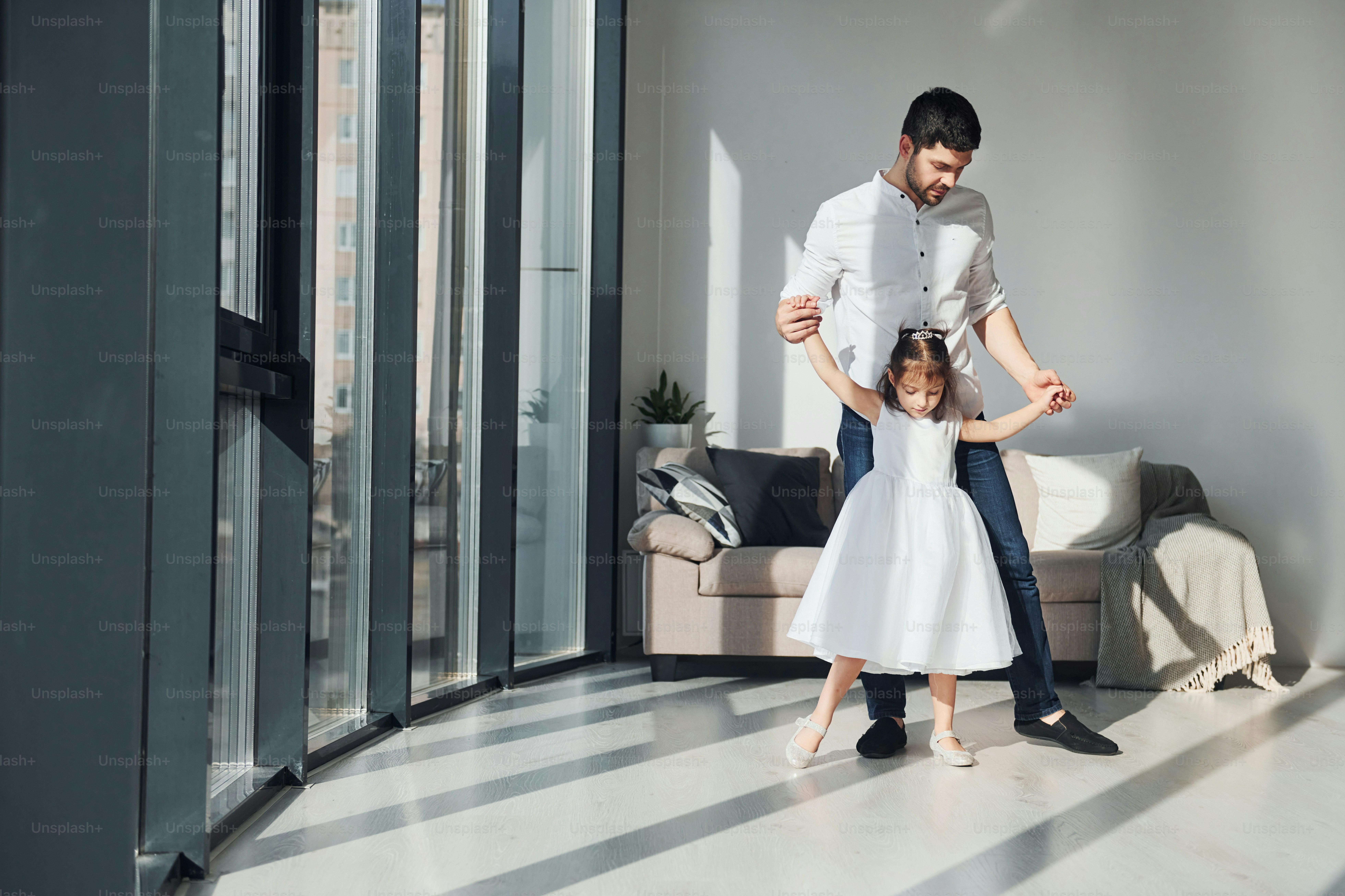 Happy father with his daughter in dress learning how to dance at home together.
