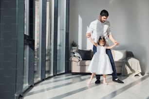 Happy father with his daughter in dress learning how to dance at home together.