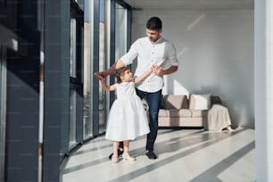 Happy father with his daughter in dress learning how to dance at home together.