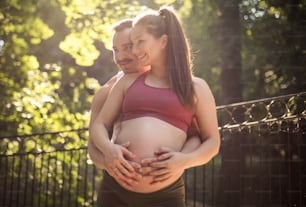 Sports couple standing in the park and touch the stomach.