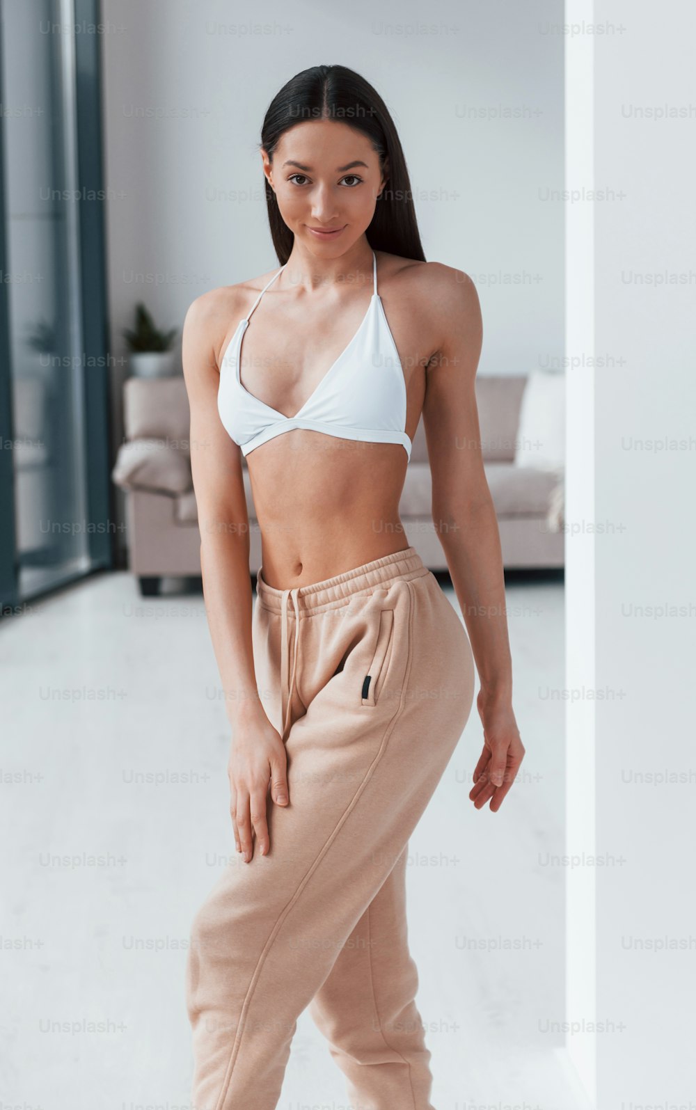 Slender woman in white underwear standing indoors in room at daytime.