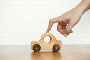 Viaje por carretera y concepto de viaje. Mano jugando con juguete de coche de madera natural sobre mesa sobre fondo de pared blanca. Espacio para el texto. Juguete ecológico sin plástico para niños pequeños. Juguete sencillo y elegante para niños