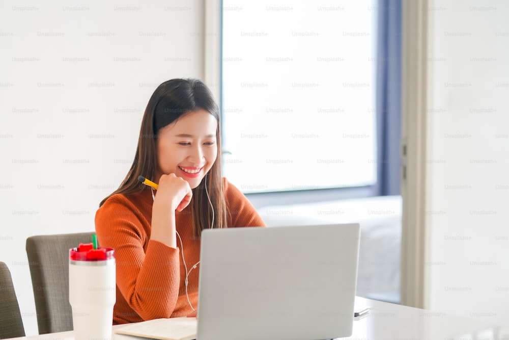 아름다운 아시아 비즈니스 여성 프리랜서는 온라인 작업을 위해 인터넷이 있는 노트북 컴퓨터를 사용하거나 집에서 메모장에 글을 쓰는 가상 세미나를 사용합니다. 자신감 여성 학습 및 화상 통화 온라인 학습 과정