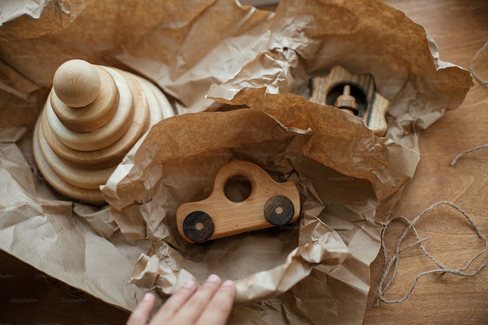 Elegantes juguetes de madera simples para niños en papel artesanal sobre mesa de madera. Regalo ecológico, pirámide moderna de madera natural con anillas, mordedor erizo y coche de juguete. Juguetes ecológicos sin plástico para niños pequeños