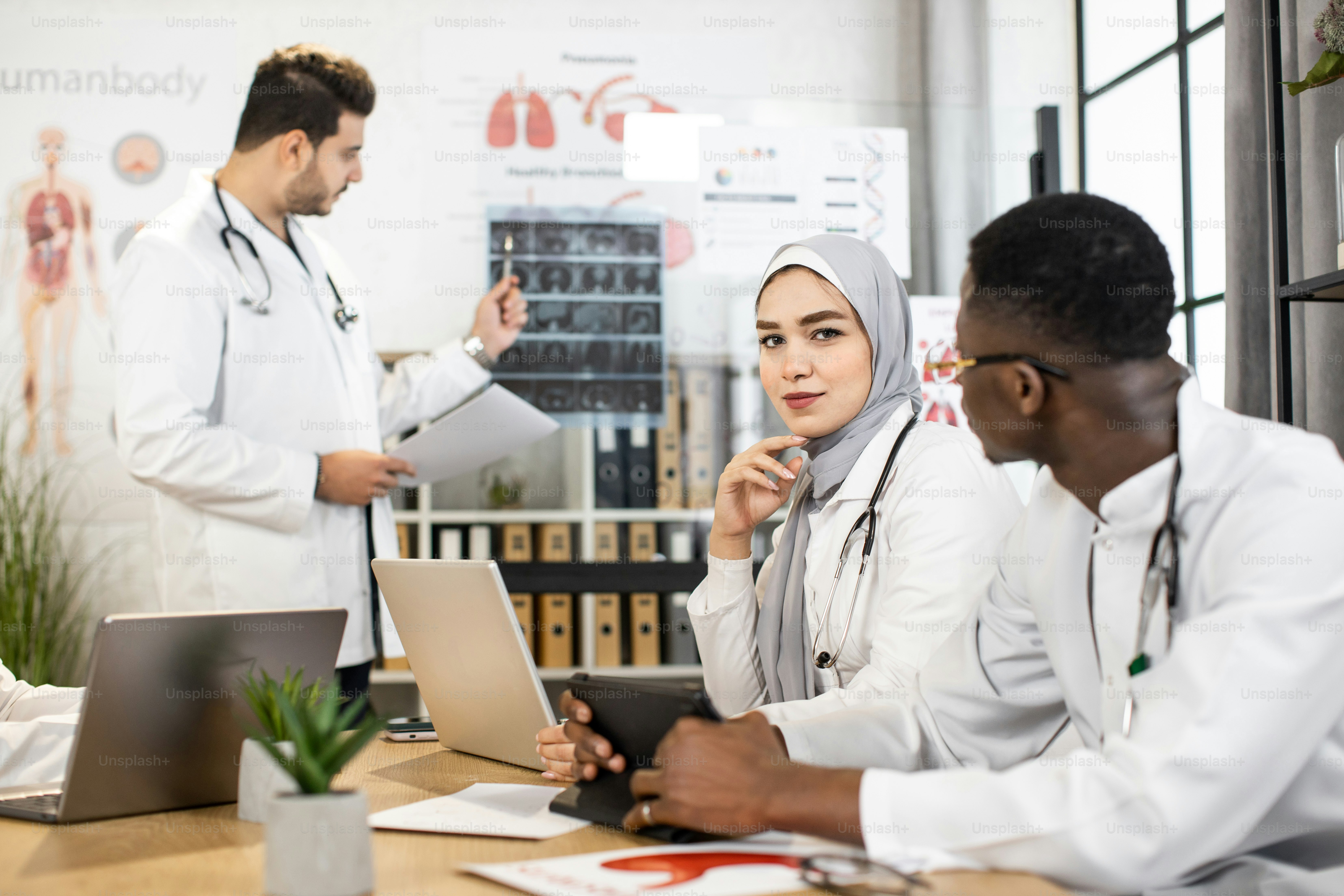 Group of four multiracial doctors using modern gadgets while examining ...