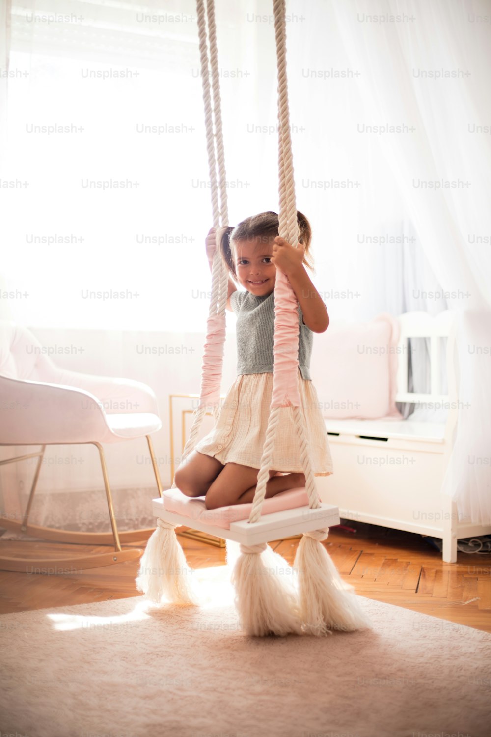 Portrait of smiling little girl on swing in her bedroom.