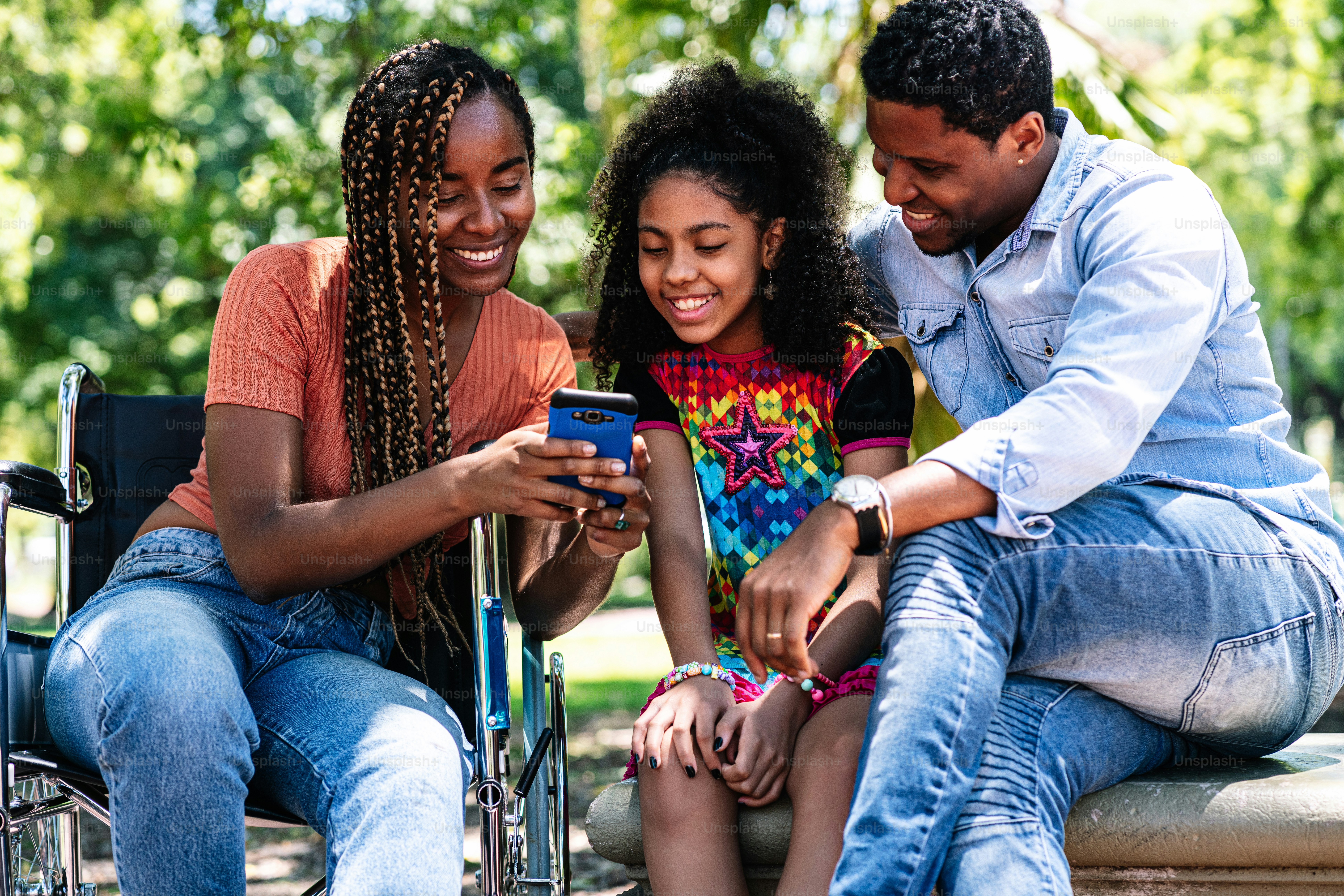 An african american woman in a wheelchair enjoying a day at the park with her family while using a mobile phone together.