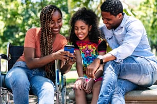 Uma mulher afro-americana em uma cadeira de rodas desfrutando de um dia no parque com sua família enquanto usavam um telefone celular juntos.