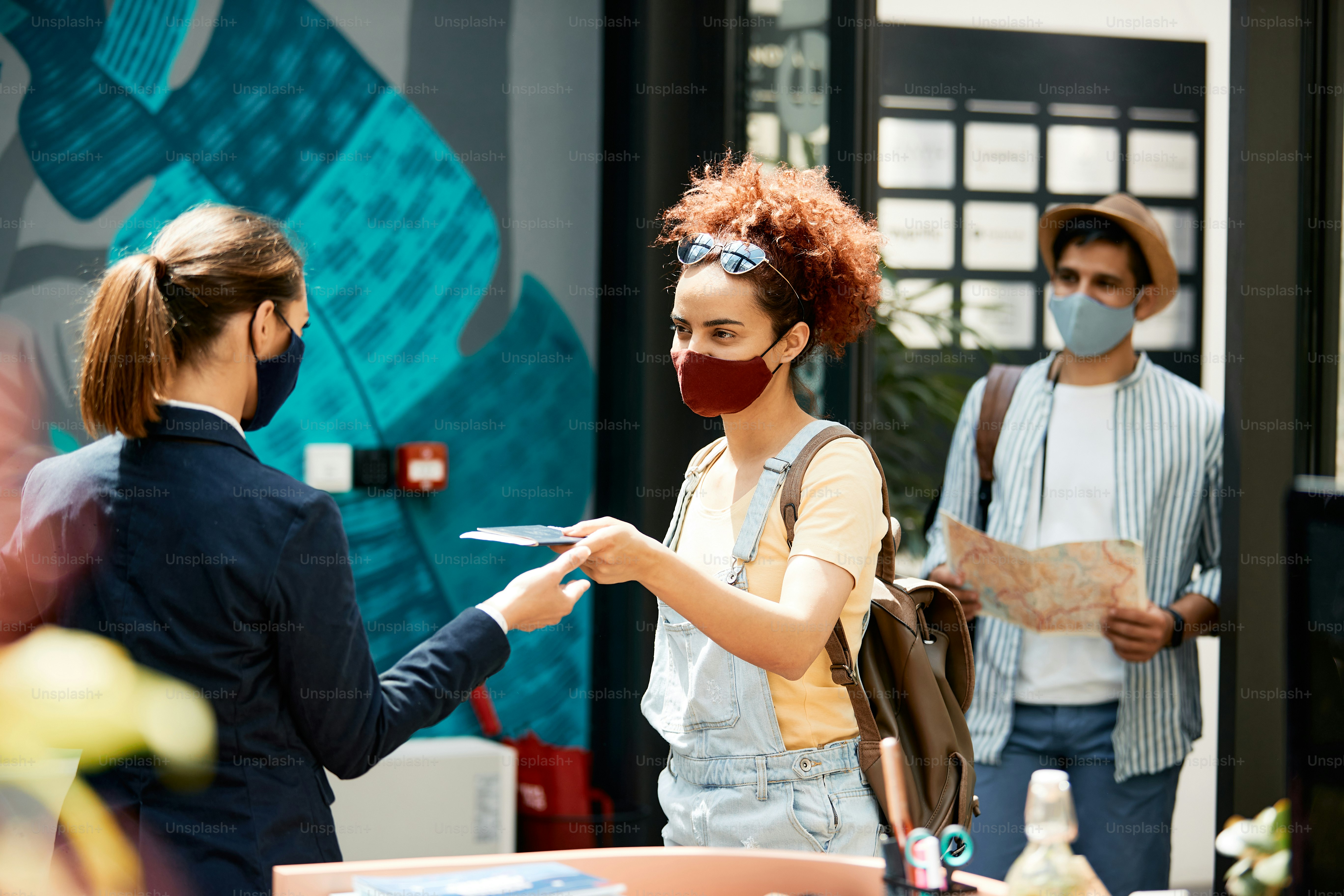 Young woman and her boyfriend arriving in hotel and giving passport to receptionist while traveling during COVID-19 pandemic.