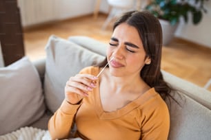 自宅でコロナウイルスPCR検査をしながら綿棒を使用する女性。コロナウイルス迅速診断検査を使用している女性。COVID-19のために鼻腔ぬぐい液を使用している自宅で若い女性。