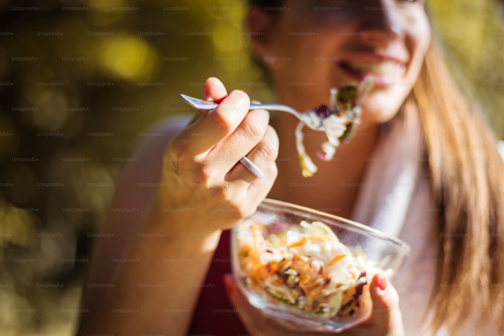 Woman eating salad in the park. Focus is on hand.