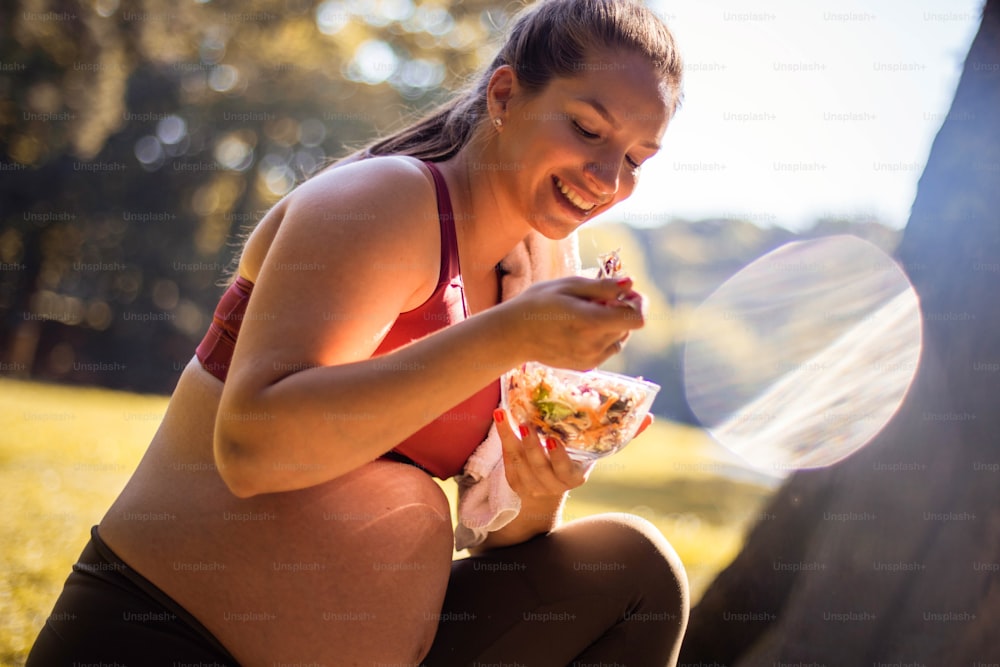 Pregnant woman eating salad after exercise in the park.