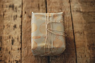 Stylish christmas gift wrapped in grey paper with thread on rustic wooden table. Happy holidays. Merry Christmas and Happy New Year. Simple xmas present