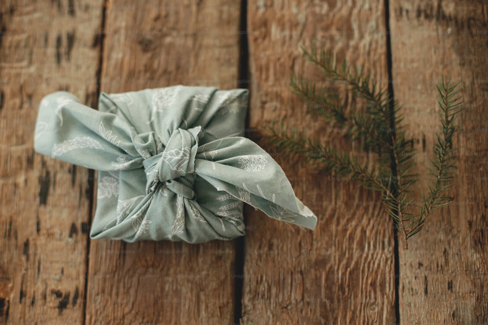Vacaciones de invierno zero waste y regalo. Regalo ecológico de Furoshiki. Elegante regalo de Navidad envuelto en tela y rama de abeto sobre mesa de madera rústica plana. Felices fiestas y Feliz Navidad