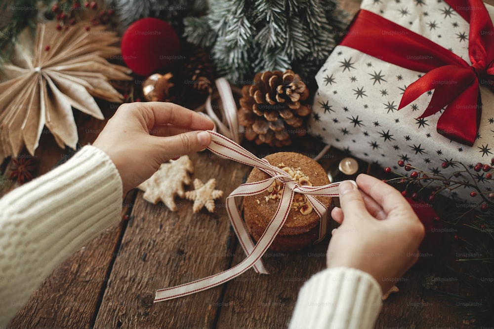 Fita amarrada de mãos em biscoitos de aveia de Natal em mesa de madeira rústica com decorações festivas elegantes. Imagem atmosférica de Natal. Biscoitos saudáveis, presentes e decoração de Natal. Boas Festas