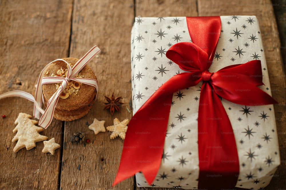 Christmas oatmeal cookies and stylish wrapped gift box with red ribbon on rustic wooden table. Xmas healthy cookies and present. Happy Holidays and Merry Christmas