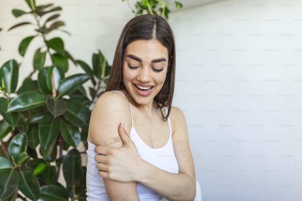 Woman pointing at his arm with a bandage after receiving the covid-19 vaccine. Young woman showing her shoulder after getting coronavirus vaccine