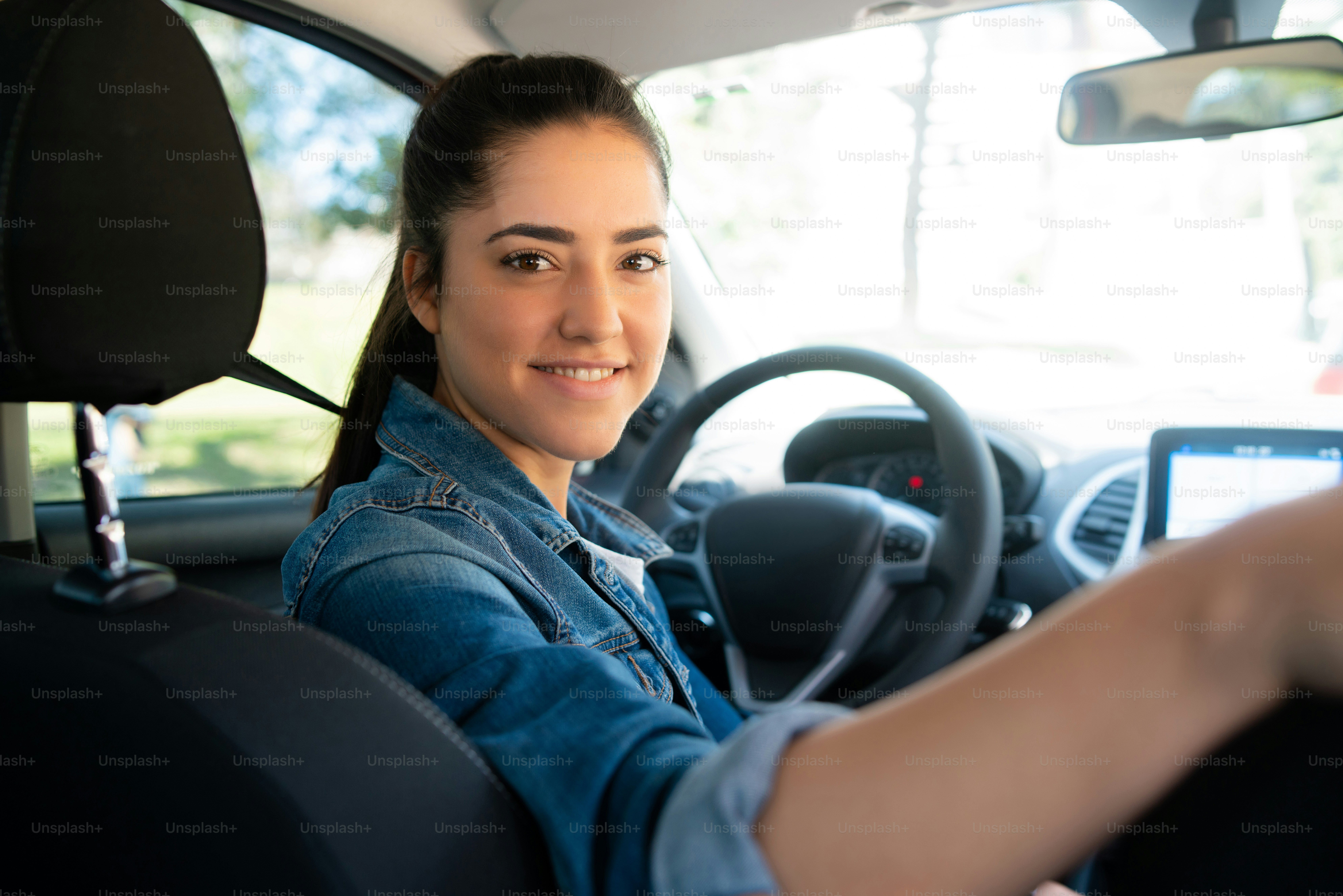 Porträt einer jungen Frau, die ihr Auto fährt und auf den Rücksitz zur Kamera schaut. Verkehrskonzept.