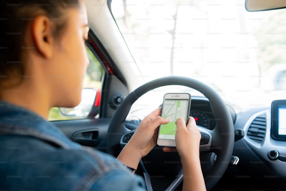 Ritratto di giovane donna che utilizza il sistema di navigazione gps sul suo telefono cellulare mentre guida la sua auto. Concetto di trasporto e navigazione.