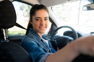 Retrato de una mujer joven conduciendo su coche y mirando al asiento trasero a la cámara. Concepto de transporte.