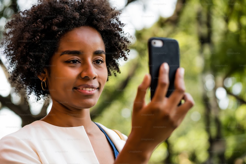 Portrait of afro business woman having a video call on mobile phone while standing outdoors at park. Urban and business concept.