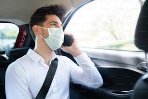 Portrait of businessman wearing face mask and talking on phone on way to work in a car. Business concept. New normal lifestyle concept.