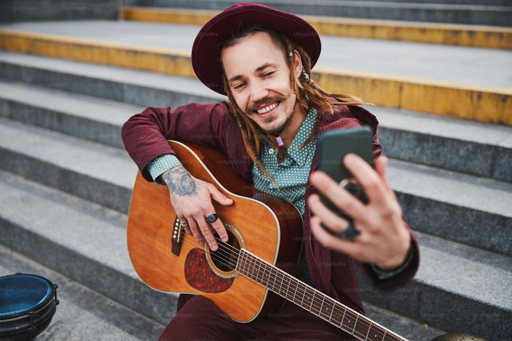 Fröhlicher Straßenmusiker demonstriert sein Lächeln beim Fotografieren mit Frontkamera