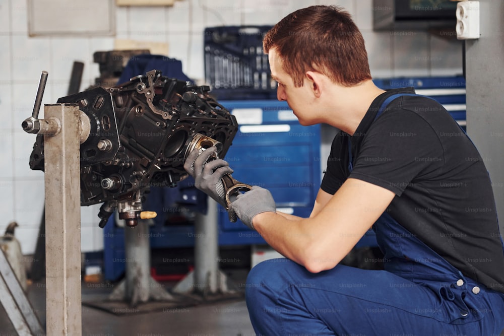 Professional repairman in garage works with broken automobile engine.