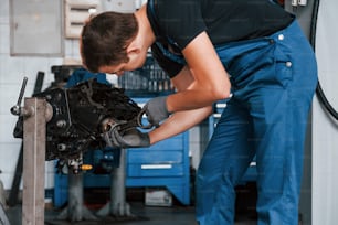 Professional repairman in garage works with broken automobile engine.