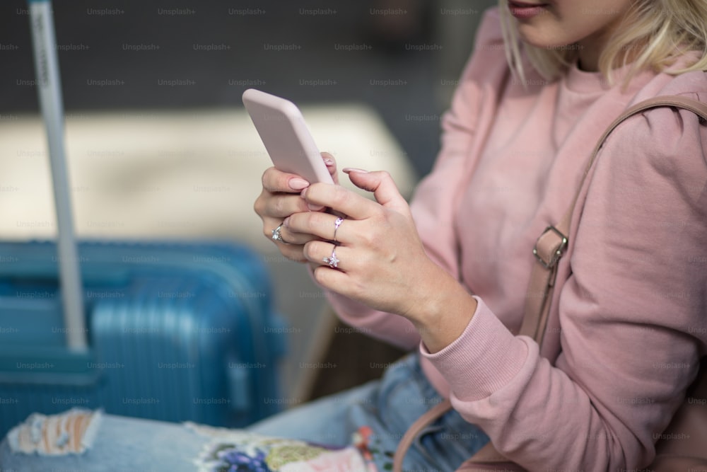Woman sitting on bus station and using mobile. Focus is on hands.