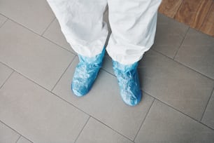 Legs of medical worker that standing indoors on the grey plate.