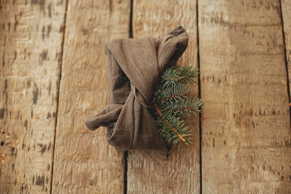Elegante regalo di Natale avvolto in tessuto con ramo di abete su tavolo in legno rustico con vista. Vacanze invernali a rifiuti zero e regalo. Furoshiki regalo ecologico. Buone feste e Buon Natale