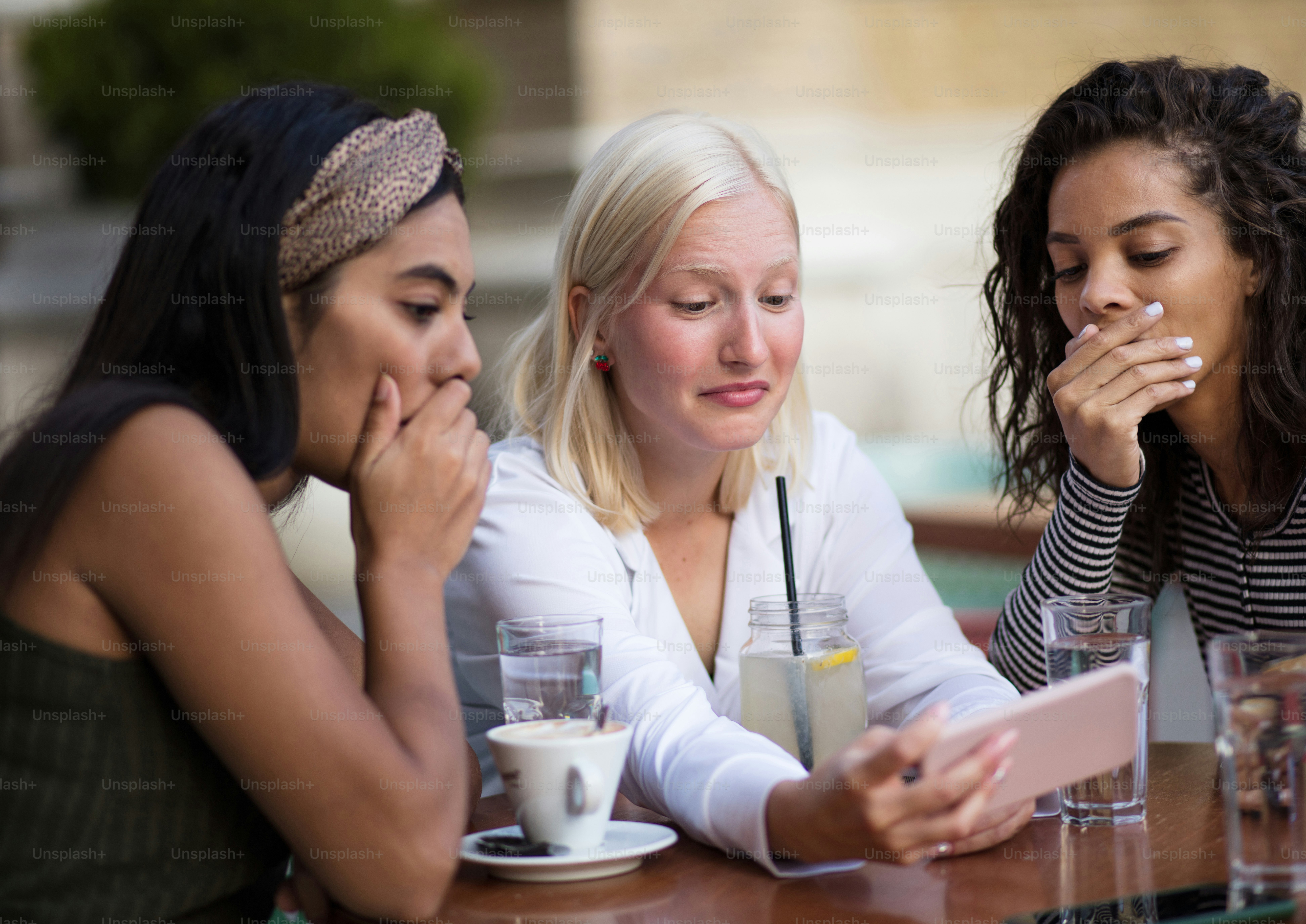 Three women sitting in café on street and talking. Using smart phone.