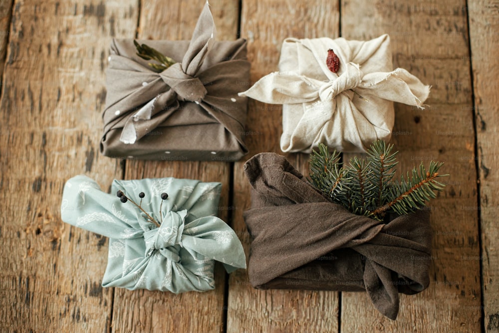 Regali a spreco zero flat lay. Furoshiki regali semplici ecologici. Eleganti regali di Natale avvolti in tessuto con ramo di abete e bacche su tavolo rustico in legno. Buone feste e Buon Natale
