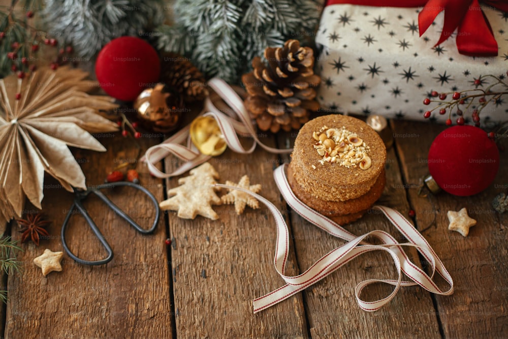 Elegante composizione natalizia d'atmosfera. Biscotti di Natale, regalo, decorazioni festive su tavolo di legno rustico. Presente di Natale, biscotti di farina d'avena sani, ornamenti. Immagine lunatica delle vacanze