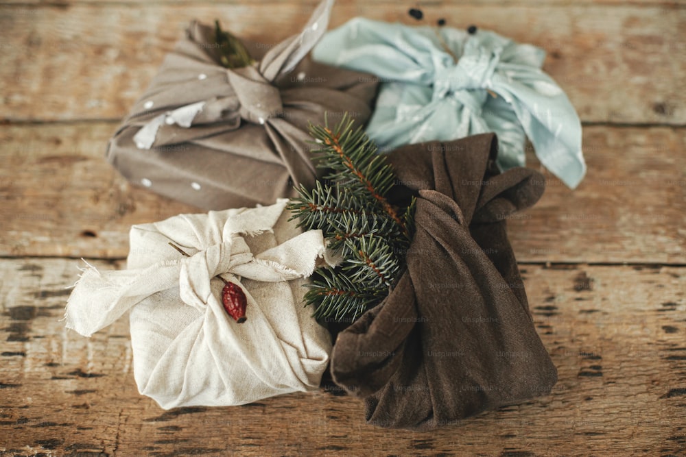 Zero waste stylish christmas gifts. Xmas presents wrapped in fabric with fir branch and berry on rustic wooden table. Eco friendly winter holidays. Furoshiki present. Happy holidays