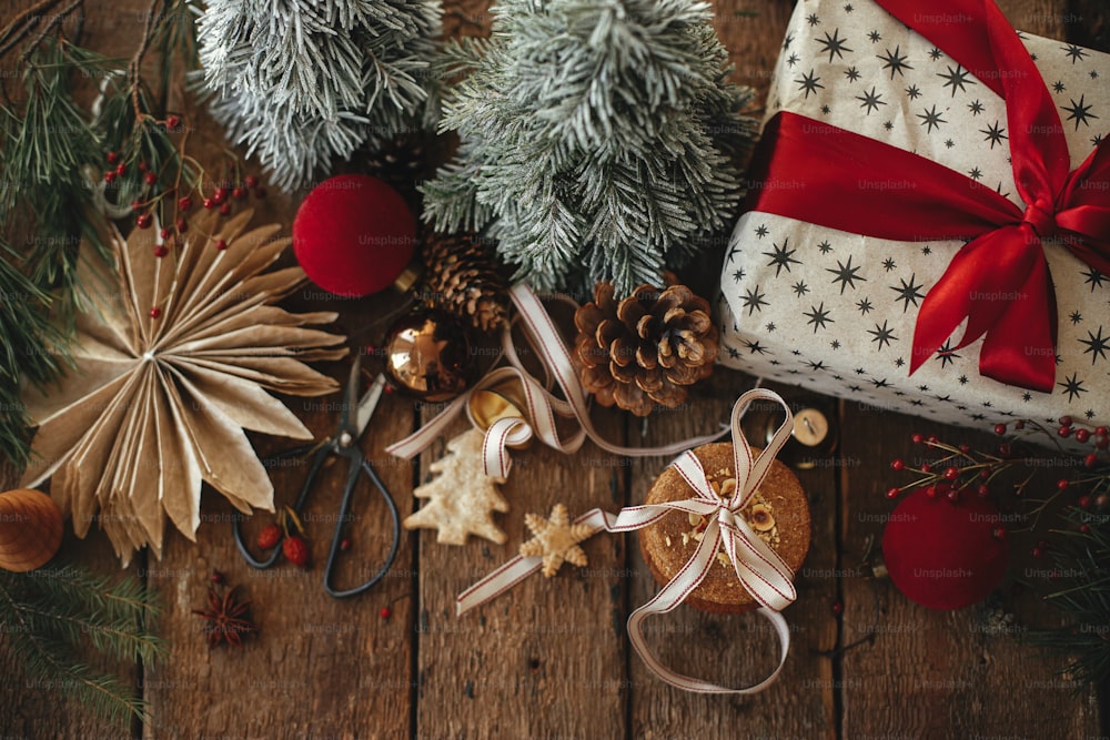 Atmosphärisch stilvolle Weihnachtskomposition flach legen. Weihnachtsplätzchen, Geschenk, festliche Dekoration auf rustikalem Holztisch. Weihnachtsgeschenk, gesunde Haferkekse, Ornamente. Urlaubsstimmungsvolles Bild