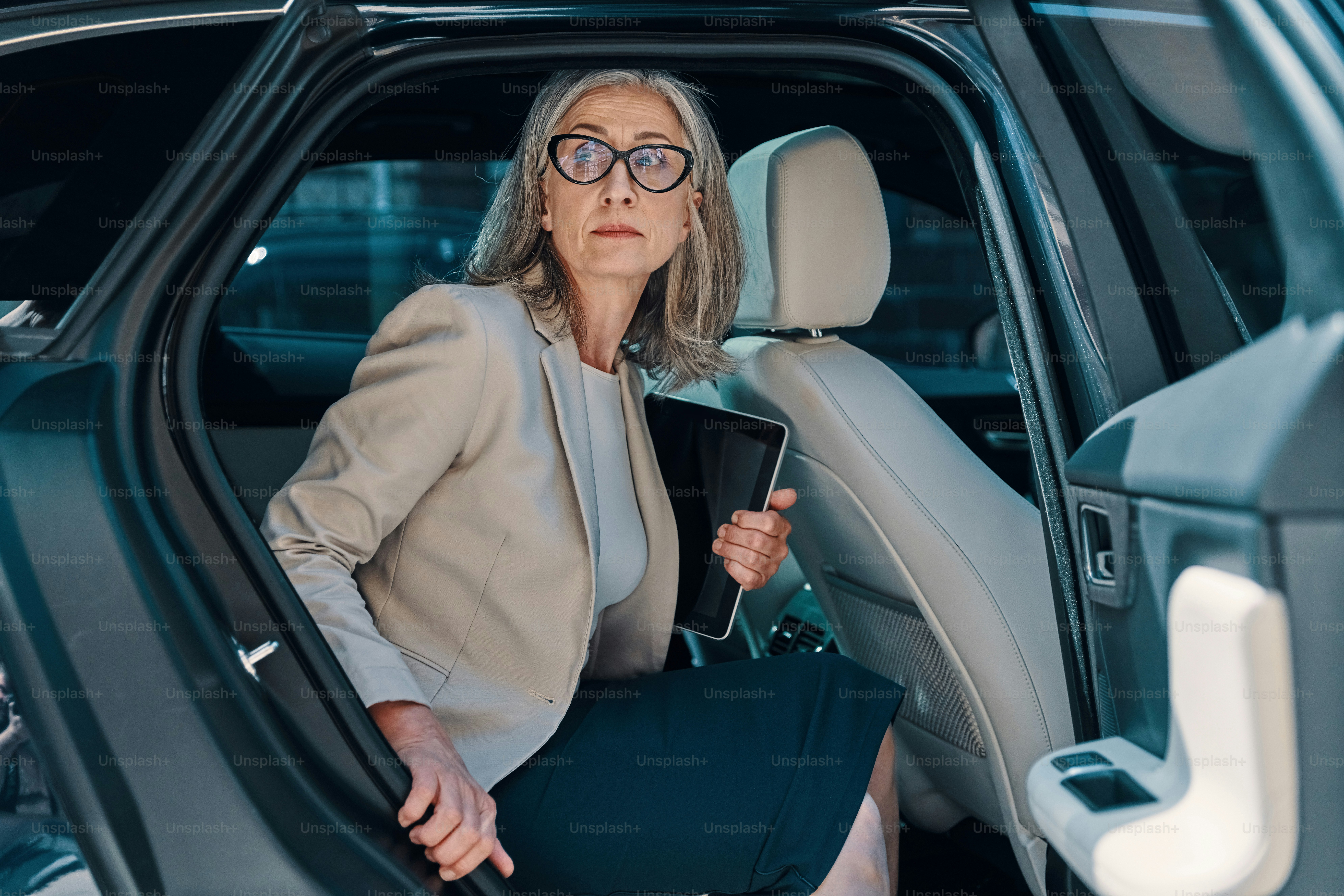 Mature beautiful woman in smart casual wear looking away while going out of the car outdoors