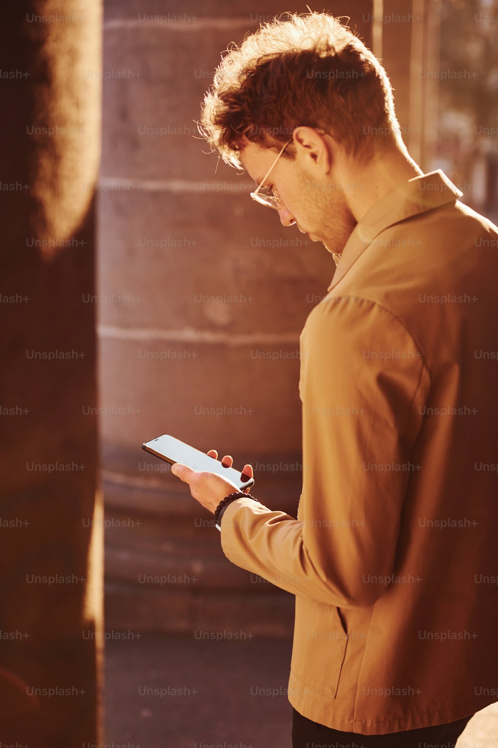Nice sunshine. Holding phone in hand. Elegant young man in formal classy clothes outdoors in the city.
