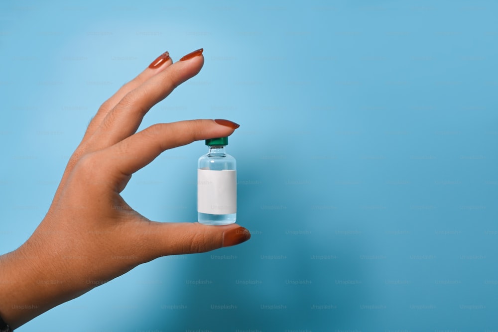 Woman holding a vaccine bottle over blue background.
